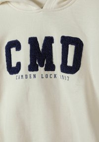 Cotton hoodie in cream, featuring navy blue terry cloth lettering "CMD" with "CAMDEN LOCK 1997" below in navy print.