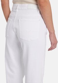 Pantaloni bianchi in denim a vita alta con tasche posteriori con dettagli di cucitura, texture morbida e etichetta sul girovita liscia.