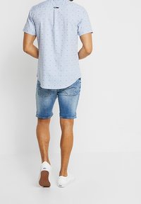 Ljusblå kortärmad skjorta med små mönstrade prickar, kombinerad med jeansshorts och vita sneakers med strukturerade sulor.