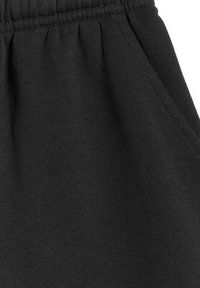 Gros plan sur un pantalon de jogging en tissu noir avec une taille élastique et des coutures visibles sur la poche latérale.