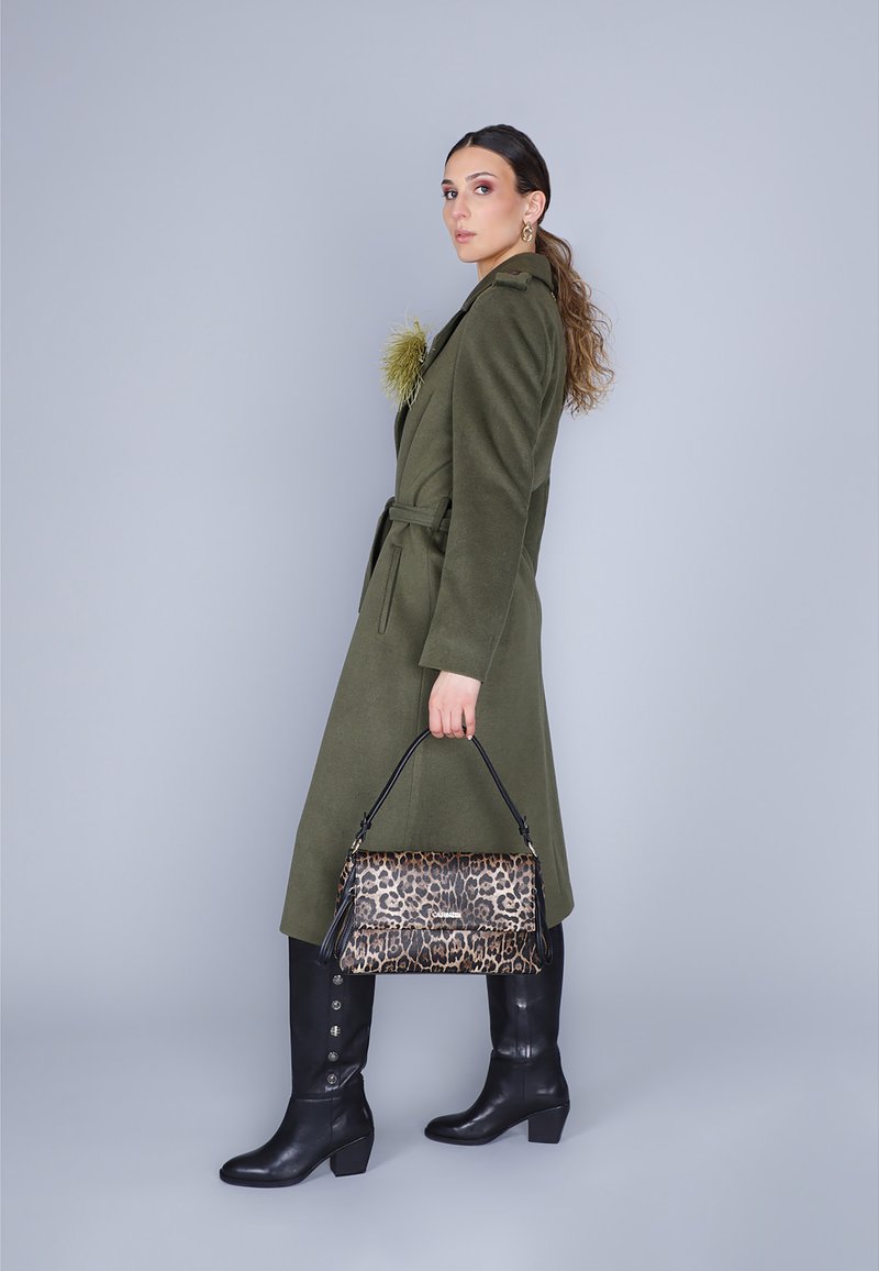 Cappotto verde oliva con vita cintata, abbinato a una borsa con stampa leopardata e stivali neri fino al ginocchio con dettagli a bottoni.