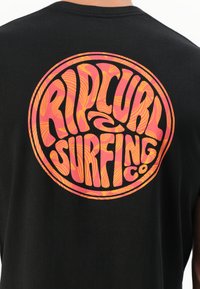 Svart bomull t-skjorte med et sirkulært grafisk design i rosa og oransje, med "Rip Curl Surfing Co" skrevet i fet, bølgete skrifttype.