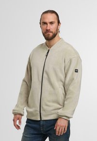 Lichtbeige fleecejack met rits, ronde hals, zijzakken en ribgebreide manchetten. Gladde textuur en minimalistisch ontwerp.