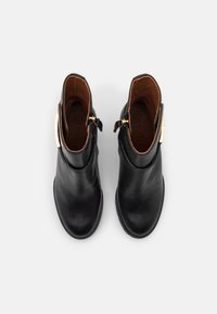 Botas de tobillo de cuero negro con una textura suave, punta redondeada y accesorios de hardware dorado. Forradas con cuero marrón para mayor comodidad.