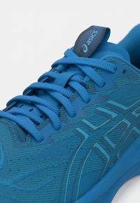 Mėlynas sportinis batelis su tekstūruotu viršumi, plokščios raištelės, paminkštintas liežuvis ir logotipas ant lipduko. Lygus pado išorė su raštuotu piešiniu.