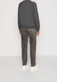 Felpa grigia scura con polsini a coste, abbinata a jeans grigi sbiaditi con dettagli di cucitura e sneakers bianche. Design semplice e casual.