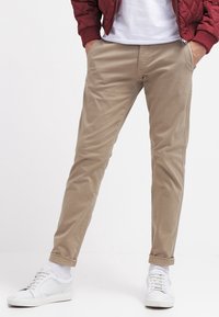Beige chinos med smal passform, tillverkade i mjukt bomullstyg, med standardfickor och uppvikta fållar, kombinerade med vita sneakers.