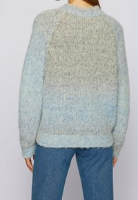 Lichtblauw gradient trui van een fuzzy breimateriaal, met een geribbelde zoom en raglan mouwen, gedragen met donkerblauwe jeans.