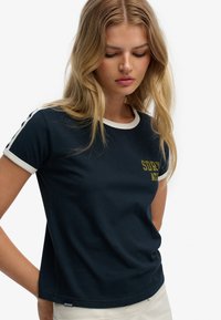 Marineblauw T-shirt met witte kraag en mouwaccenten, met de opdruk "SDRY" en "AT" in geel. Gemaakt van een zachte katoenmix.