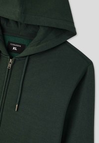 Felpa con zip di colore verde scuro realizzata in tessuto morbido. Dotata di cappuccio regolabile con coulisse, zip in metallo e di un'etichetta con la scritta "TERRANOVA XL".
