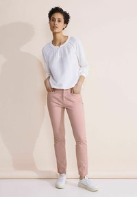 Vit texturerad långärmad blus med en nyckelhållsringning, i kombination med ljusrosa smala byxor och vita sneakers.