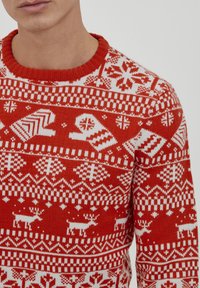 Pull en laine rouge avec des motifs de Noël blancs, y compris des rennes et des gants, avec un col rond côtelé et un design texturé.
