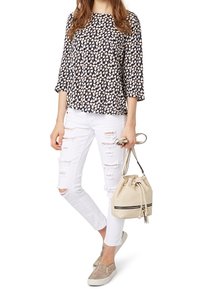 Blusa blu navy con motivo crema, maniche 3/4; jeans skinny bianchi con effetto distressed; borsa a secchiello beige; scarpe slip-on glitterate.