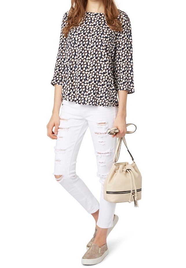 Blusa blu navy con motivo crema, maniche 3/4; jeans skinny bianchi con effetto distressed; borsa a secchiello beige; scarpe slip-on glitterate.