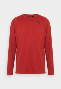 Langärmliges Sportshirt aus rotem Stoff mit glatter Textur, versehen mit schwarzem Logo auf der linken Brust und Raglanärmeln.