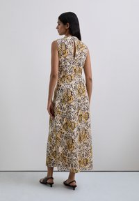 Maxikleid mit Blumenmuster und einem runden Ausschnitt auf der Rückseite, das einen gelben und lila Leopardenprint auf hellem Hintergrund zeigt, gefertigt aus leichtem Stoff.