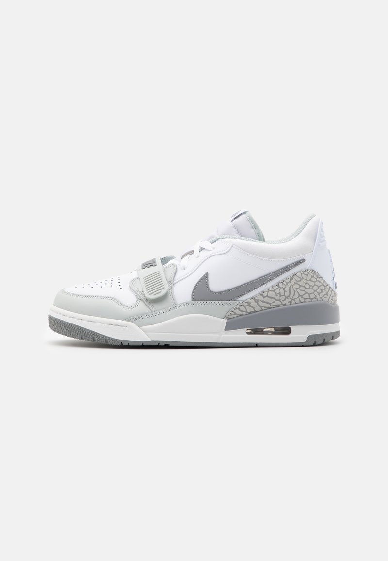 Baskets basses Nike blanches et grises avec lacets, une sangle au milieu du pied, une semelle à coussin d’air visible et un imprimé éléphant texturé au talon.