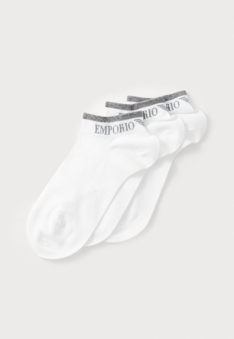 Chaussettes blanches à la cheville dans un paquet de quatre, avec un revers rayé gris portant le logo "Emporio". Le matériau semble lisse avec un léger stretch.