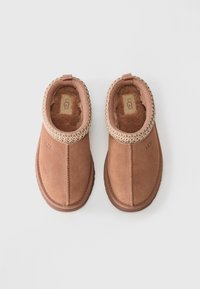 Pair of brown UGG slip-on slippers with plush lining and decorative stitching around the ankle on a white background.