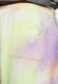 Pantalons de survêtement en mélange de coton avec un motif tie-dye pastel dans les tons de vert, violet et orange, dotés d'une seule poche plaquée à l'arrière.