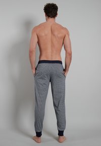 Men's pajama pants in a blue and white pattern, with a navy elastic waistband and ankle cuffs. Soft fabric with a relaxed fit.