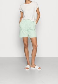 Light gray t-shirt with rolled sleeves, paired with mint green elastic waist shorts. White slide sandals complete the outfit. Smooth fabric texture.