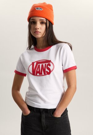 T-shirt bianca in cotone con rifiniture rosse, con un grande logo "VANS" rosso sul davanti. Abbinata a jeans neri e un berretto arancione a coste.