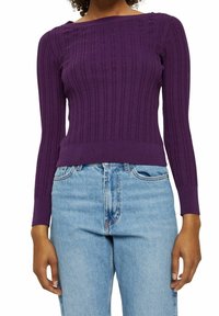 Rippstrick-Pullover in Lila mit weitem Rundhalsausschnitt und langen Ärmeln, kombiniert mit hoch taillierten hellblauen Jeans. Glatte Textur und taillierte Passform.