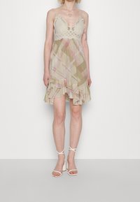 Kevyt ruudullinen mekko, jossa on spagettihihnat, pitsiyksityiskohtia vartalon kohdalla ja röyhelöhelma beigeillä sävyillä, joissa on vaaleanpunaisia ja vihreitä yksityiskohtia.