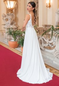 Abito da sposa bianco con un corpetto ricamato in pizzo e schiena bassa. La gonna fluente si estende fino al pavimento, posizionata contro uno sfondo interno lussuoso.