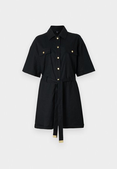 Robe-shirt noire à manches courtes avec un devant boutonné, deux poches poitrine, une taille ceinturée et des boutons dorés. Fabriquée en tissu texturé.