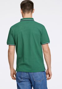 Zielona koszulka polo z teksturowanej tkaniny, z krótkimi rękawami i kołnierzykiem. Posiada kontrastowe wykończenie wzdłuż krawędzi kołnierza i rękawów.