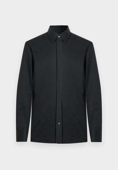 Μαύρο μακρυμάνικο πουκάμισο από λείο ύφασμα, με κωνικό γιακά, πλήρη μπροστινή κουμπότρυπα και κουμπωτές μανσέτες. Χωρίς σχέδια ή διακοσμητικά στοιχεία.