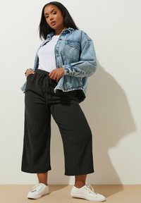 Denimjacka i ljusblått, vit t-shirt, svarta vida byxor och vita sneakers. Har en framficka och avslappnad passform.