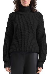 Zwarte gebreide coltrui met een gestructureerd patroon, losse pasvorm, verlaagde schouders en lange mouwen. Gecombineerd met zwarte broek.