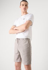 White short-sleeve t-shirt with black logo and trim. Beige linen shorts with drawstring waist and side pockets. Overall casual outfit.