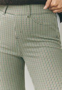 Grün-weiß karierte, maßgeschneiderte Hose mit figurbetontem Schnitt, vorderen Taschen und glatter Textur.