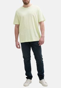 T-shirt en coton vert clair avec un col rond classique, associés à un jean bleu marine et des baskets blanches, avec une coupe décontractée.