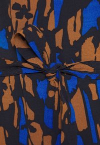 Tissu avec des formes abstraites bleues et brunes sur fond noir, noué en un nœud central.