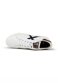 Sneaker bianca con branding X nero, dettagli marroni e lacci bianchi. Presenta una tomaia in pelle liscia e suola in gomma. Design minimalista.