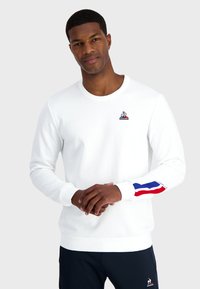 Felpa bianca in misto cotone, con colletto rotondo, maniche lunghe con strisce rosse e blu, e un piccolo logo sul petto.