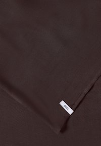 Tissu brun foncé avec des coutures visibles et une petite étiquette rectangulaire blanche portant l'inscription "CECIL" cousue dans la couture.