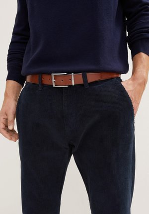 Pantalons en velours côtelé bleu marine avec des côtes verticales, associés à une ceinture en cuir marron dotée d'une boucle rectangulaire en argent et de détails de couture subtils.