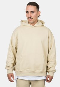 Beige hooded sweatshirt with a kangaroo pocket, ribbed cuffs, and a relaxed fit. Soft, textured fabric in a solid color.