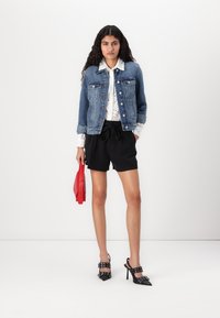 Chaqueta de denim sobre una camisa de ojo de perdiz blanca, combinada con pantalones cortos negros, zapatos de tacón negros y un bolso rojo. Un atuendo simple y casual.