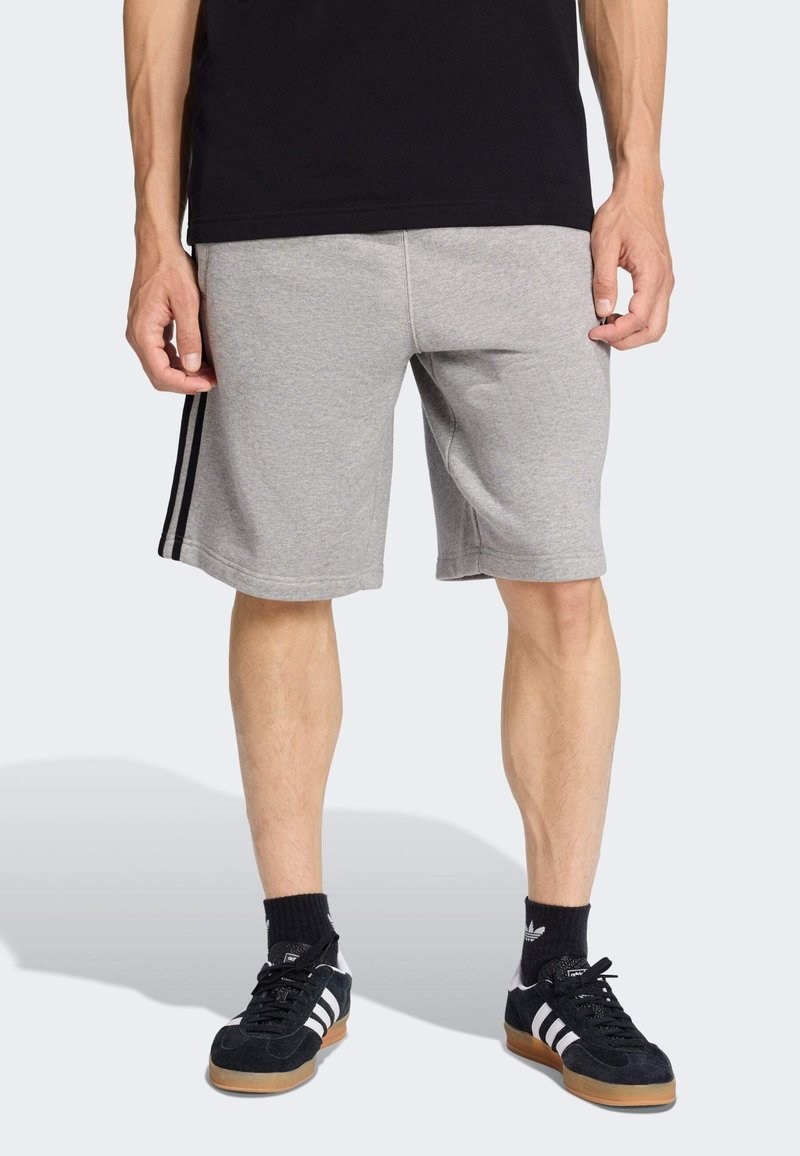 Sivé športové šortky z mäkkej látky, s čiernymi bočnými pruhmi a elastickým pásom. Nosené s čiernymi topánkami a ponožkami.