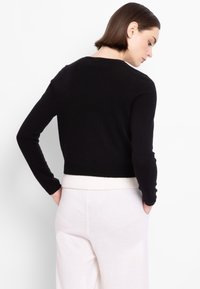Maglione corto nero con maniche lunghe e scollatura rotonda, dotato di un orlo a coste bianco. Tessuto morbido, design aderente.