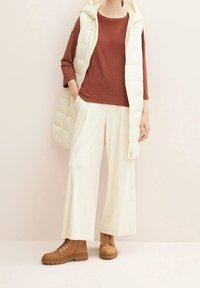 Gilet bianco gonfio, top color ruggine e pantaloni a gamba larga color crema. Stivaletti marroni alla caviglia con lacci. Tessuti morbidi, palette di colori neutri.