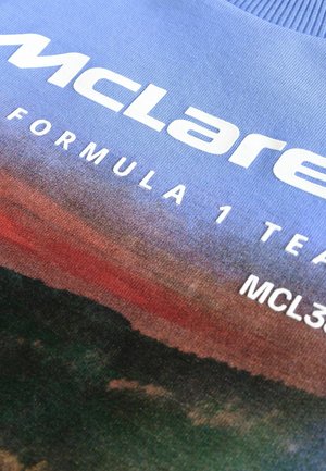 Sweatshirt de l'équipe McLaren Formula 1, avec un design dégradé en bleu, rouge et vert. Présenté avec un texte blanc en gras. Texture de tissu douce.