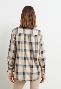 Camicia a quadri beige con righe nere, grigie e ruggine. Maniche lunghe, polsini con bottoni e dettaglio plissettato sulla schiena. Tessuto dalla texture morbida.